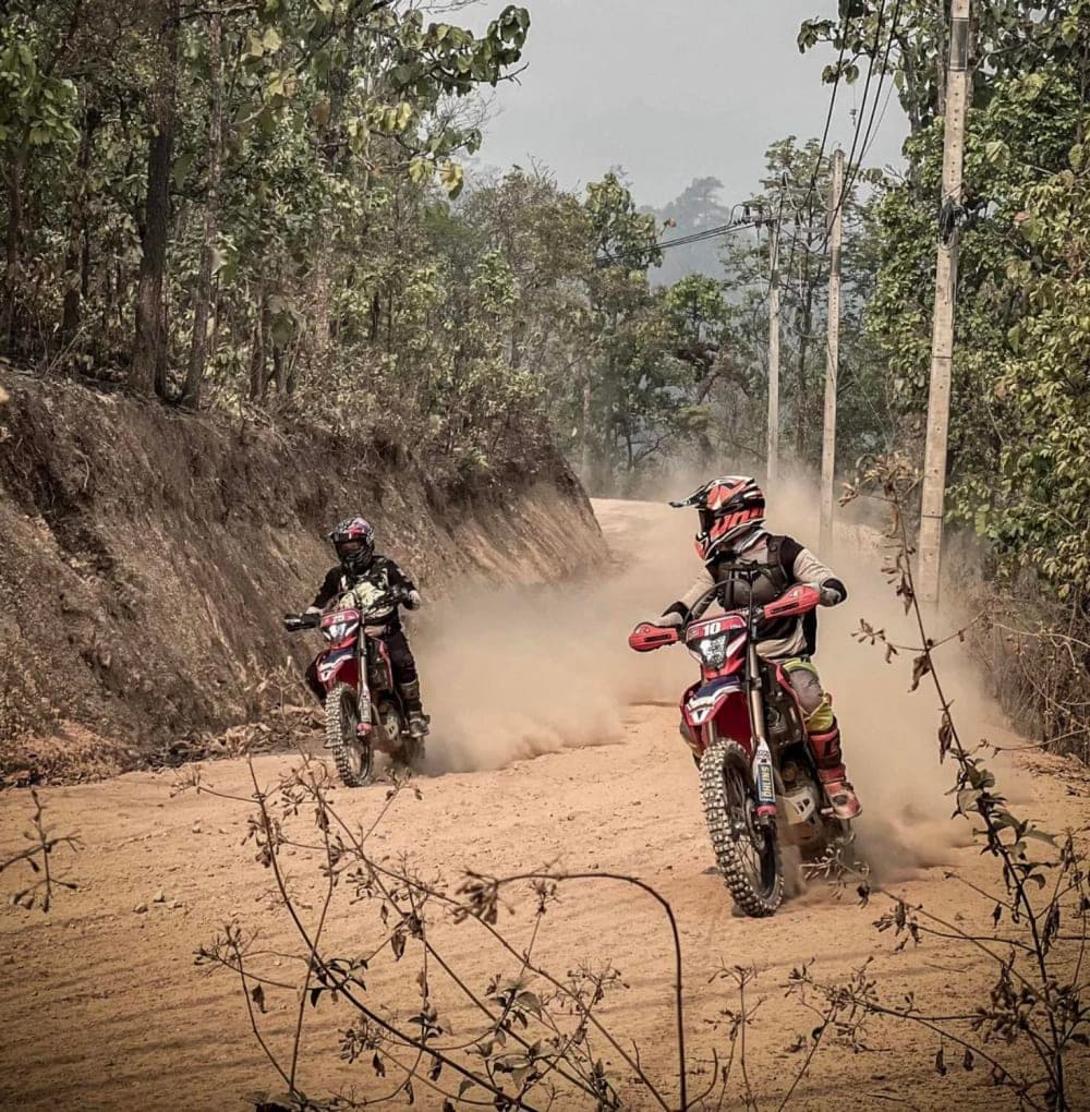 Enduro rider crossing a wide tropical river on a dirt bike in Thailand
